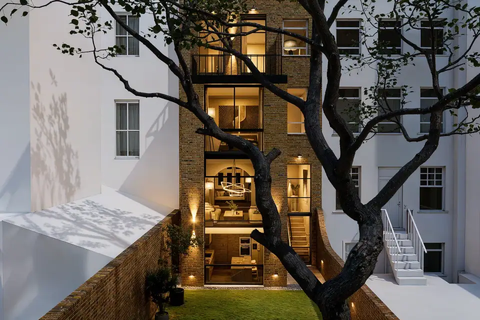 A Victorian townhouse at dusk, its glazed rear extension glowing behind a tree
