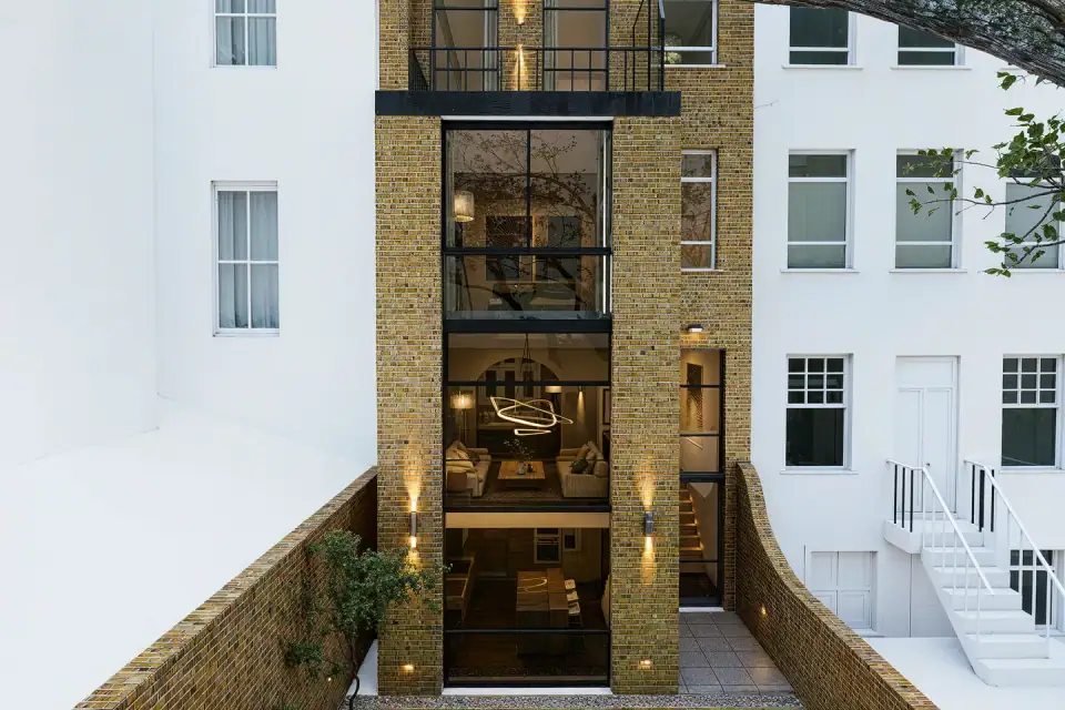 Tall glazed rear wing of a Victorian townhouse, showing lit living rooms on each floor